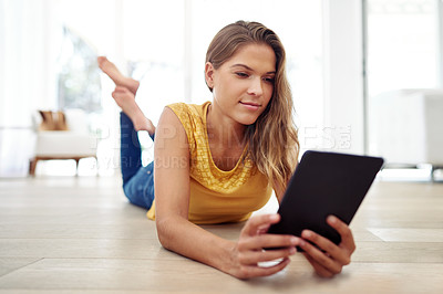 Buy stock photo Full body shot of an attractive young woman sitting and using a tablet in the living room during the day