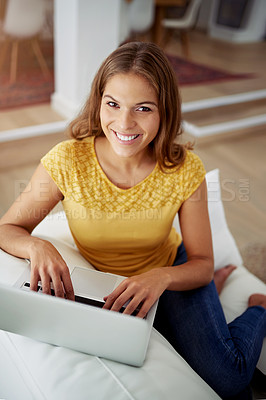 Buy stock photo Cropped portrait of an attractive young woman using a laptop while sitting on a sofa at home