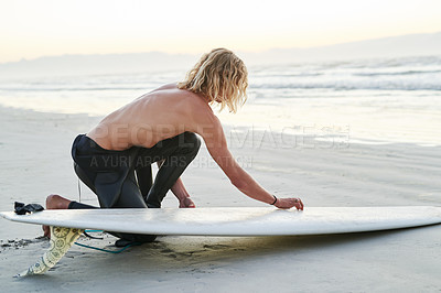 Buy stock photo Full length shot of a handsome young surfer getting his surfboard ready before going surfing at the beach