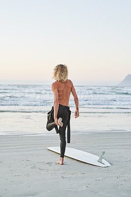 Buy stock photo Rearview shot of a young man stretching before going surfing at the beach