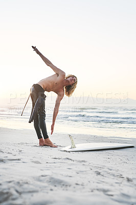 Buy stock photo Full length shot of a handsome young man stretching before going surfing at the beach