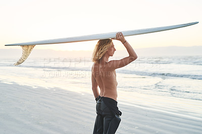 Buy stock photo Shot of a young surfer carrying his surfboard over his head as he gets ready to surf at the beach