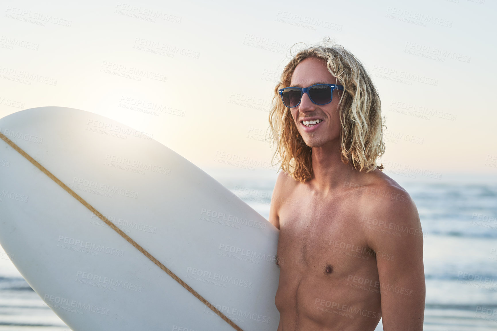 Buy stock photo Shot of a handsome young man carrying his surfboard at the beach