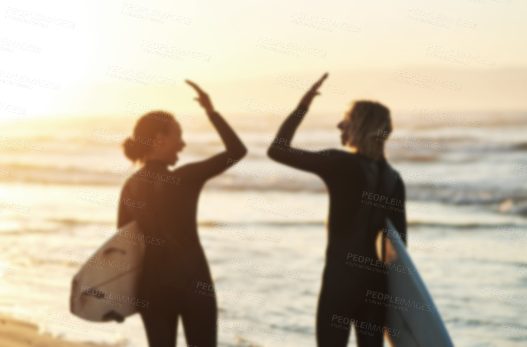 Buy stock photo Rearview shot of a young couple joining hands for a high five while surfing at the beach