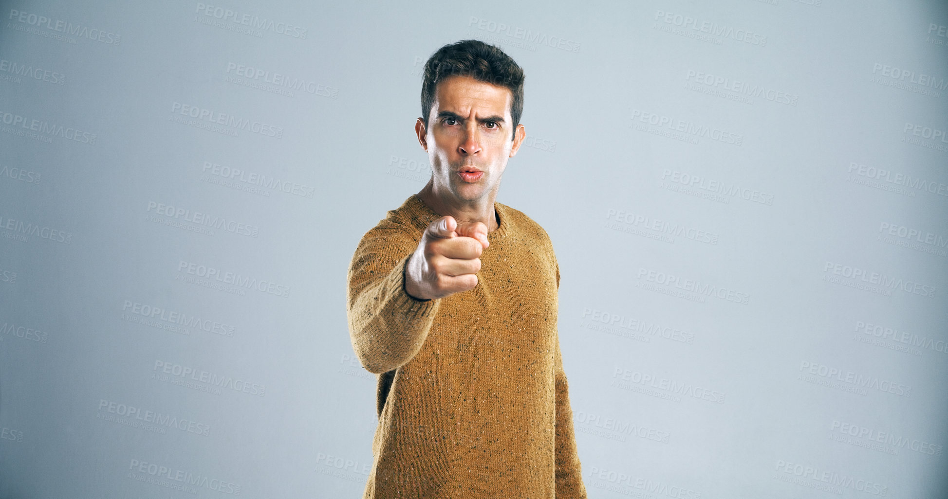 Buy stock photo Studio shot of a handsome young man pointing a finger in anger against a gray background