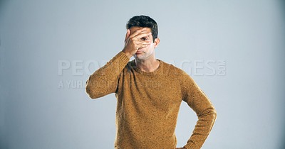 Buy stock photo Studio shot of a young man covering his eyes in disappointment against a gray background