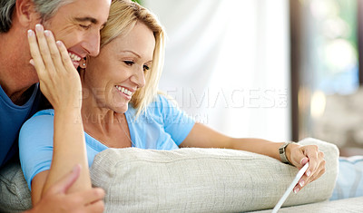 Buy stock photo Cropped shot of an affectionate mature couple using a digital tablet while sitting on the sofa at home