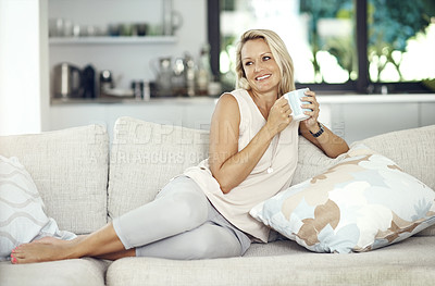 Buy stock photo Full length shot of an attractive mature woman enjoying a warm beverage while relaxing on the sofa at home