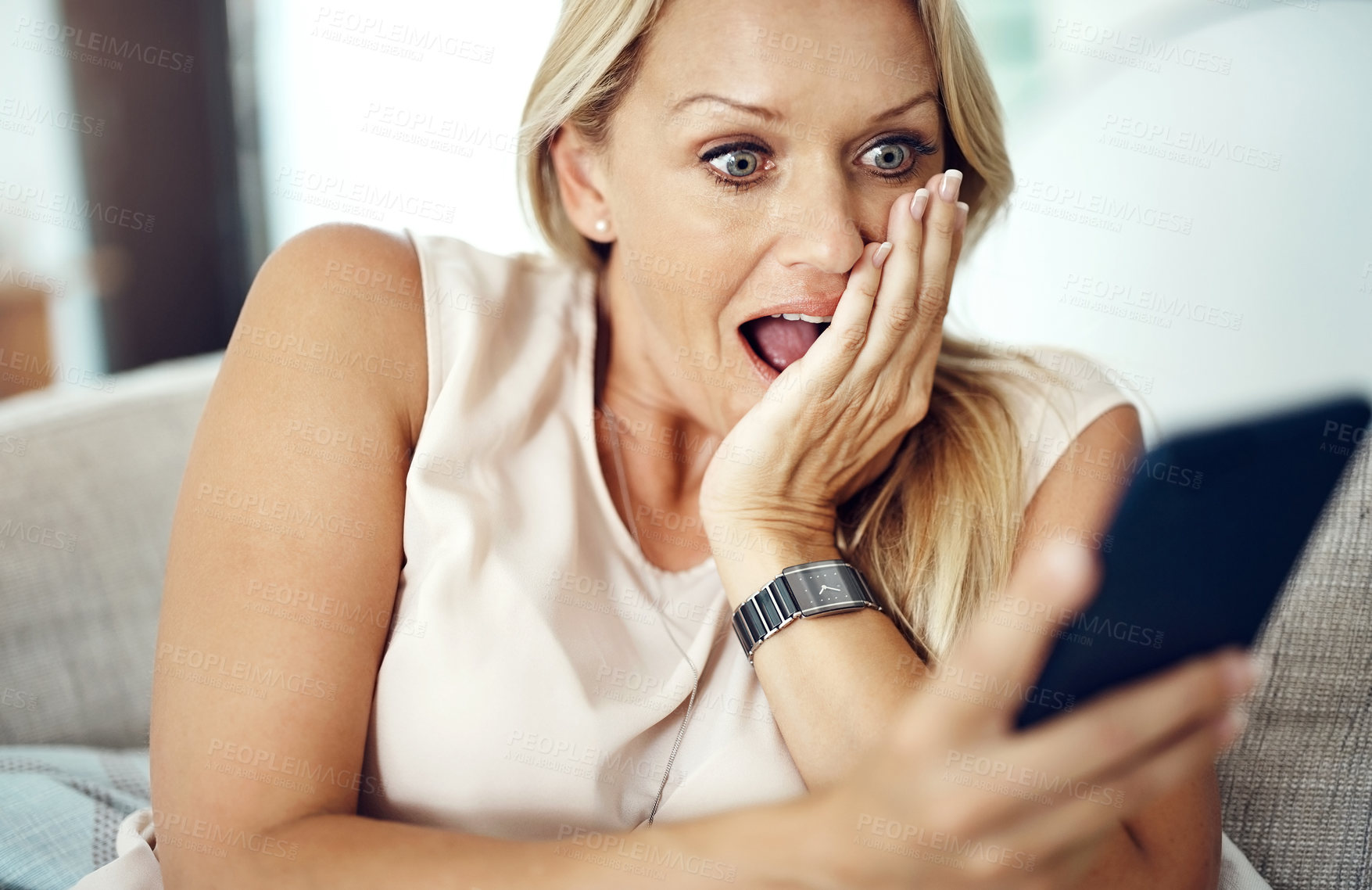 Buy stock photo Cropped shot of an attractive mature woman looking surprised while reading a text message at home