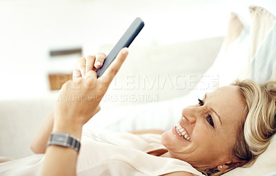 Buy stock photo Cropped shot of an attractive mature woman reading a text message while relaxing on the sofa at home