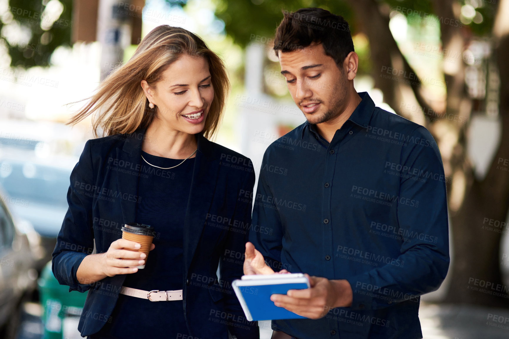 Buy stock photo Cropped shot of two corporate colleagues having a discussion while walking down the street on their way to work