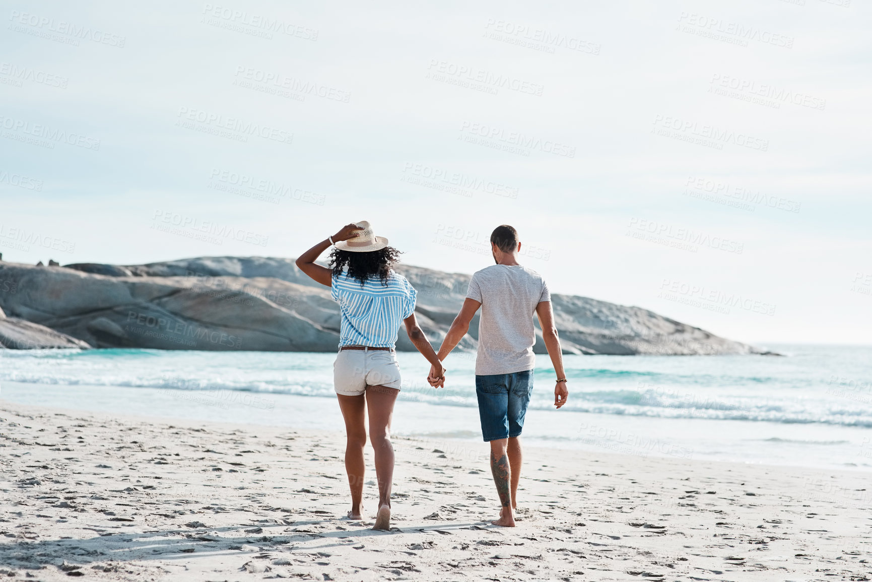 Buy stock photo Rearview shot of a young couple walking along the beach