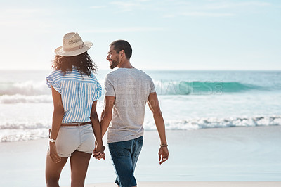 Buy stock photo Rearview shot of a young couple walking along the beach