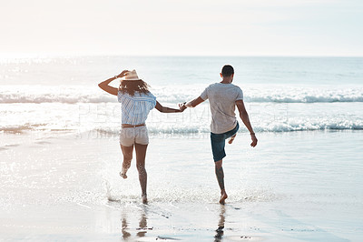 Buy stock photo Beach, play and couple for romance, honeymoon and travel for fun, kick and splashing. African woman, holding hands or sea on date to show partner adventure, happiness or bonding or joy on holiday