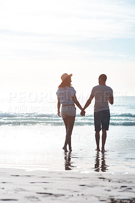 Buy stock photo Rearview shot of a young couple walking along the beach