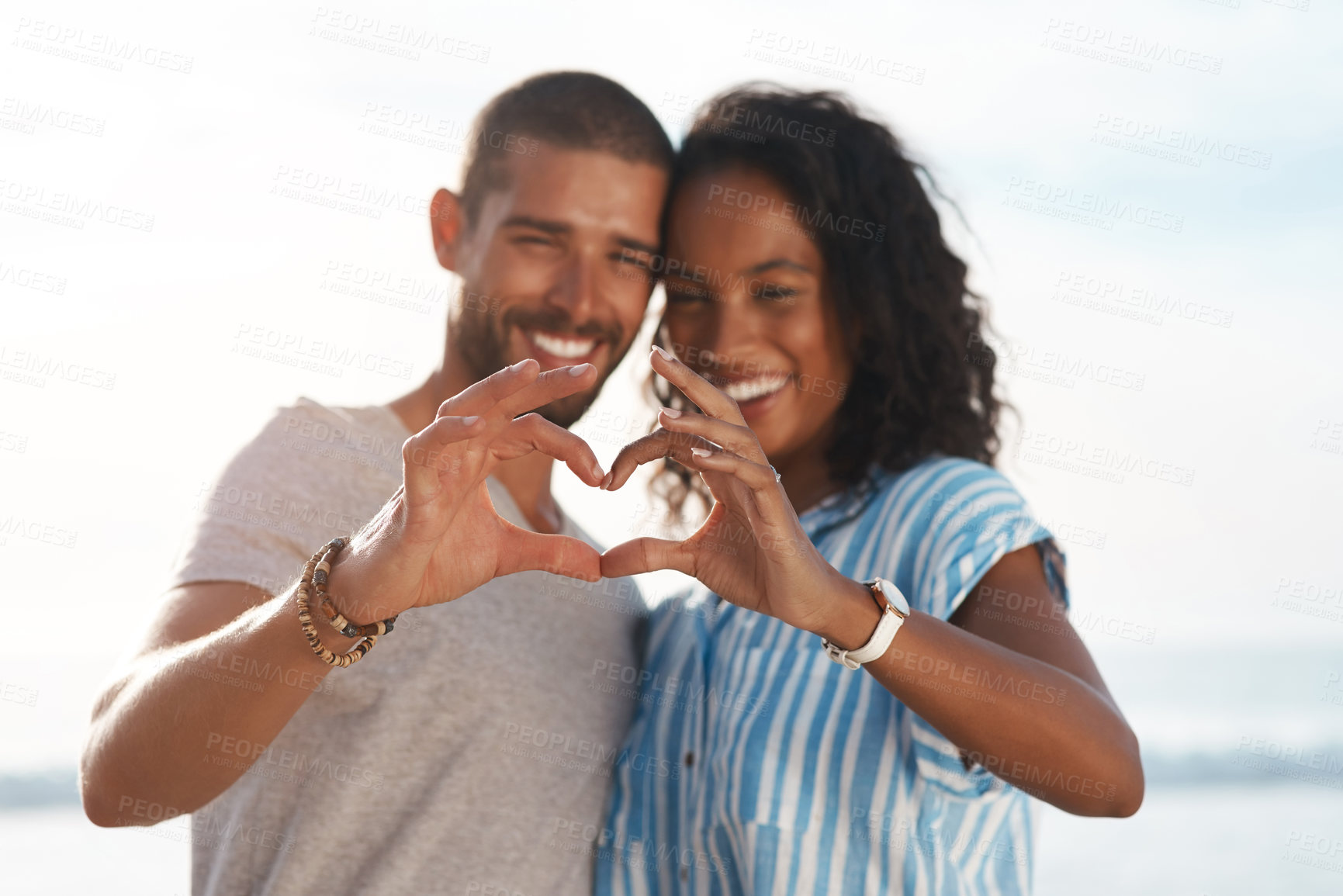Buy stock photo Shot of a young couple making a heart shape with their hands at the beach