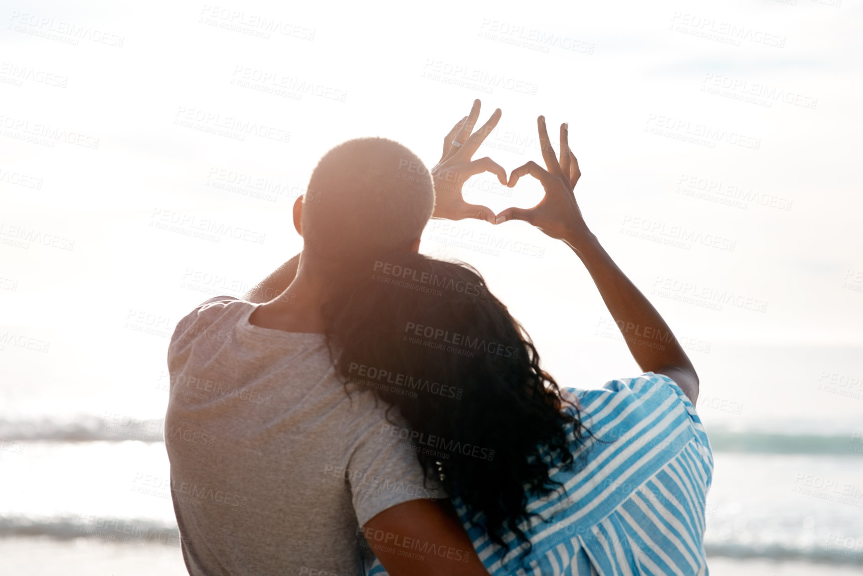 Buy stock photo Rearview shot of a young couple making a heart shape with their hands at the beach