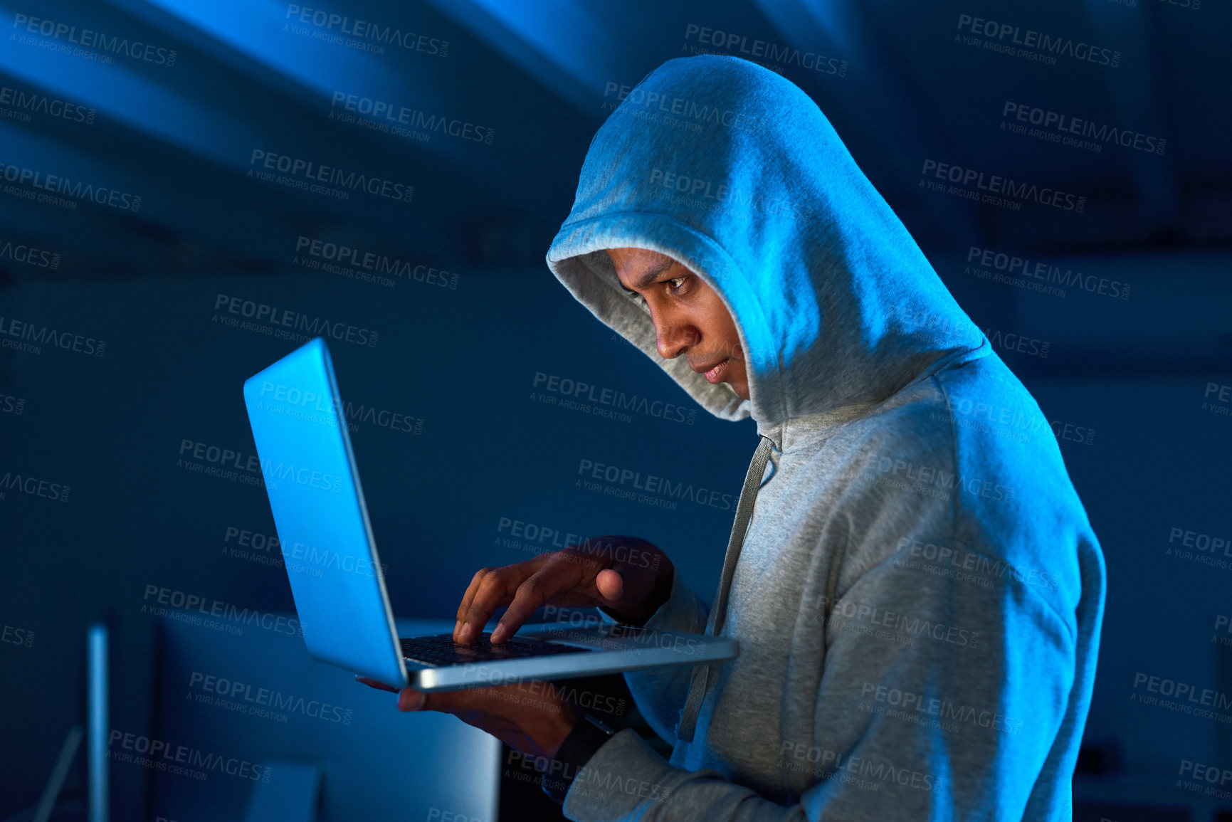 Buy stock photo Shot of a young male hacker using a laptop in the dark