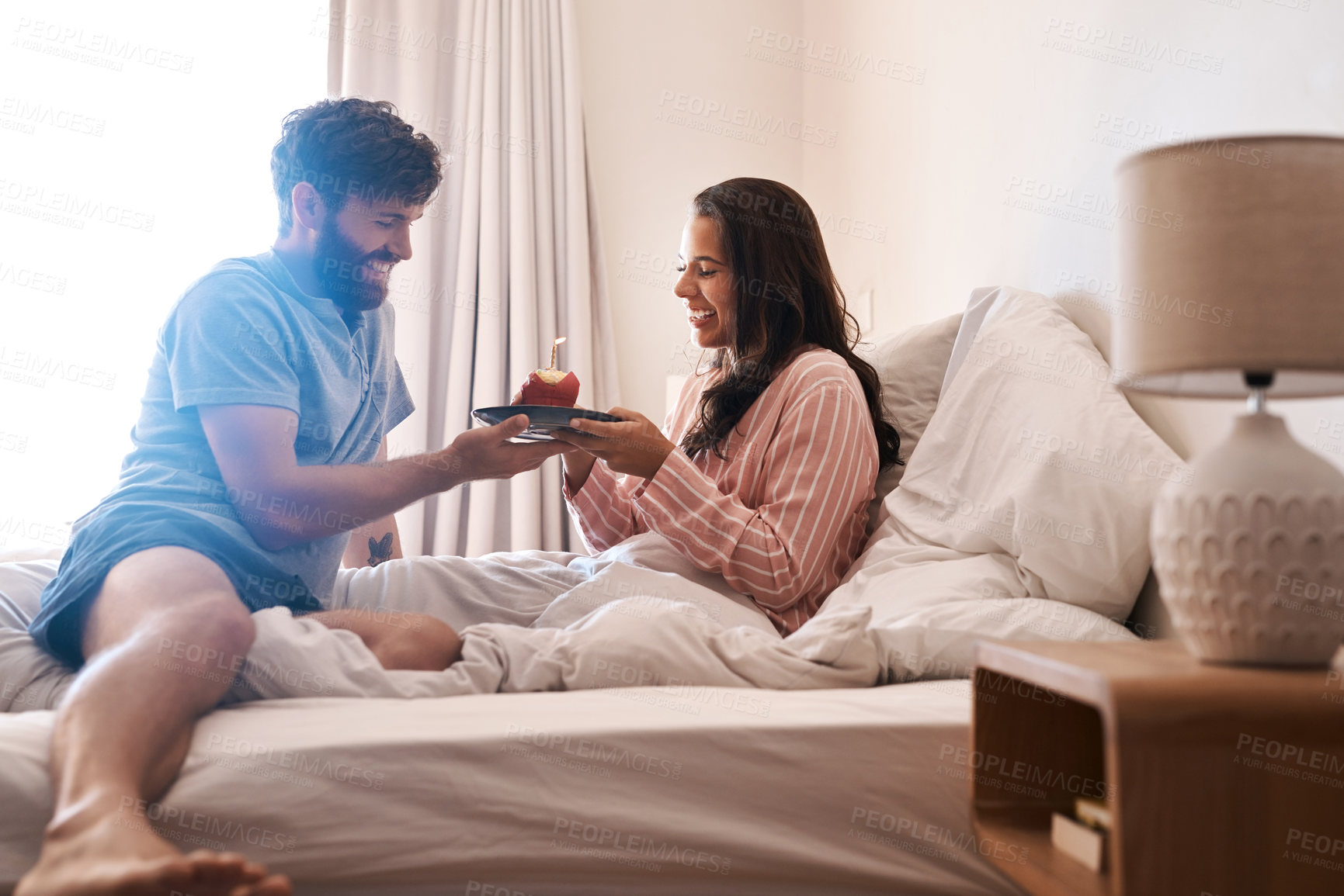 Buy stock photo Happy couple, bedroom and birthday muffin, morning dessert or celebration food for excited woman. Cupcake candle, surprise sweets and fun people smile, happiness and celebrate special day on home bed