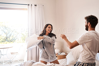 Buy stock photo Shot of a happy young couple having a pillow fight in bed