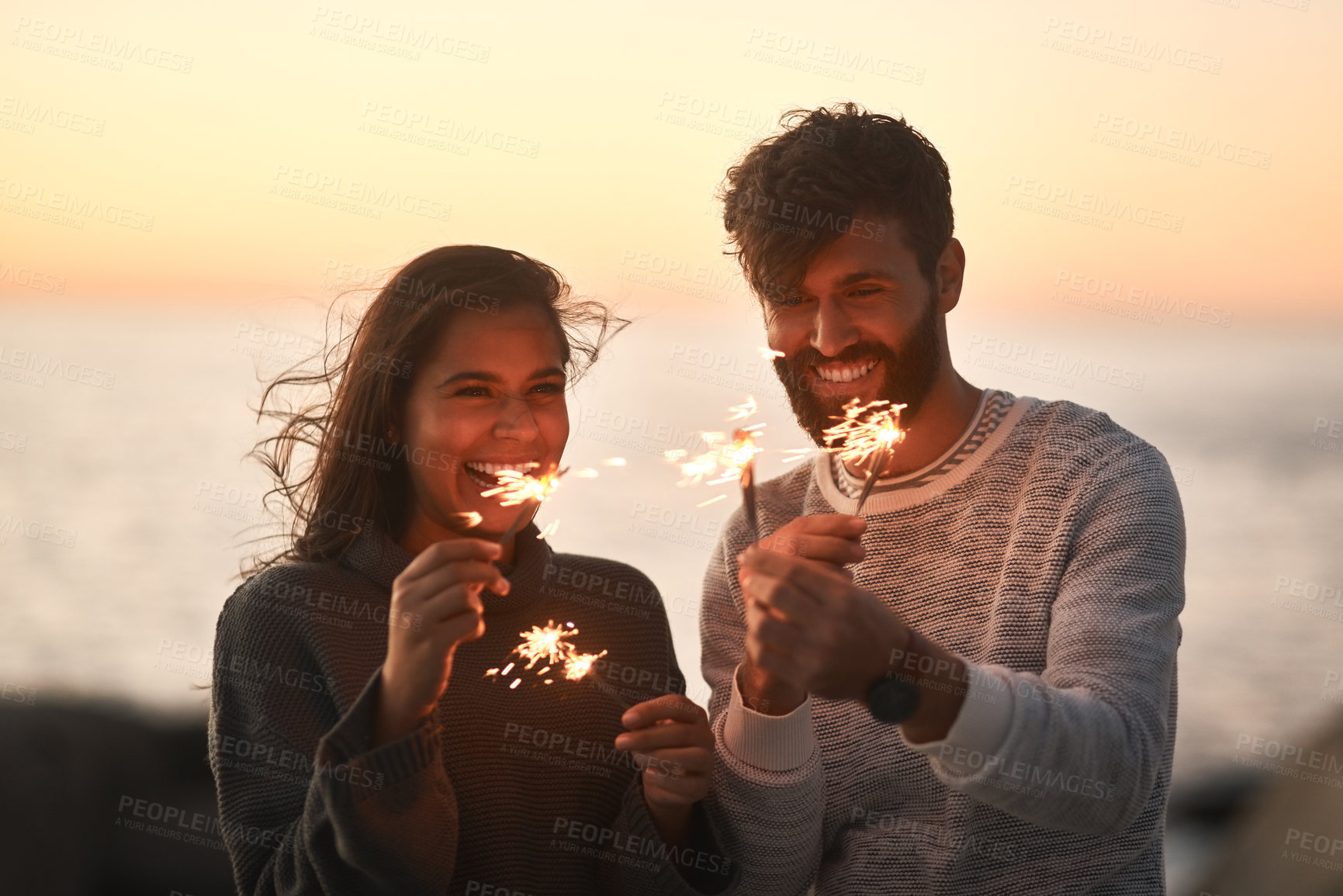 Buy stock photo Sunset, beach and couple with fireworks for celebration, party and sparks on romantic date. Nature, love and happy man and woman with sparklers for honeymoon on holiday, weekend and vacation