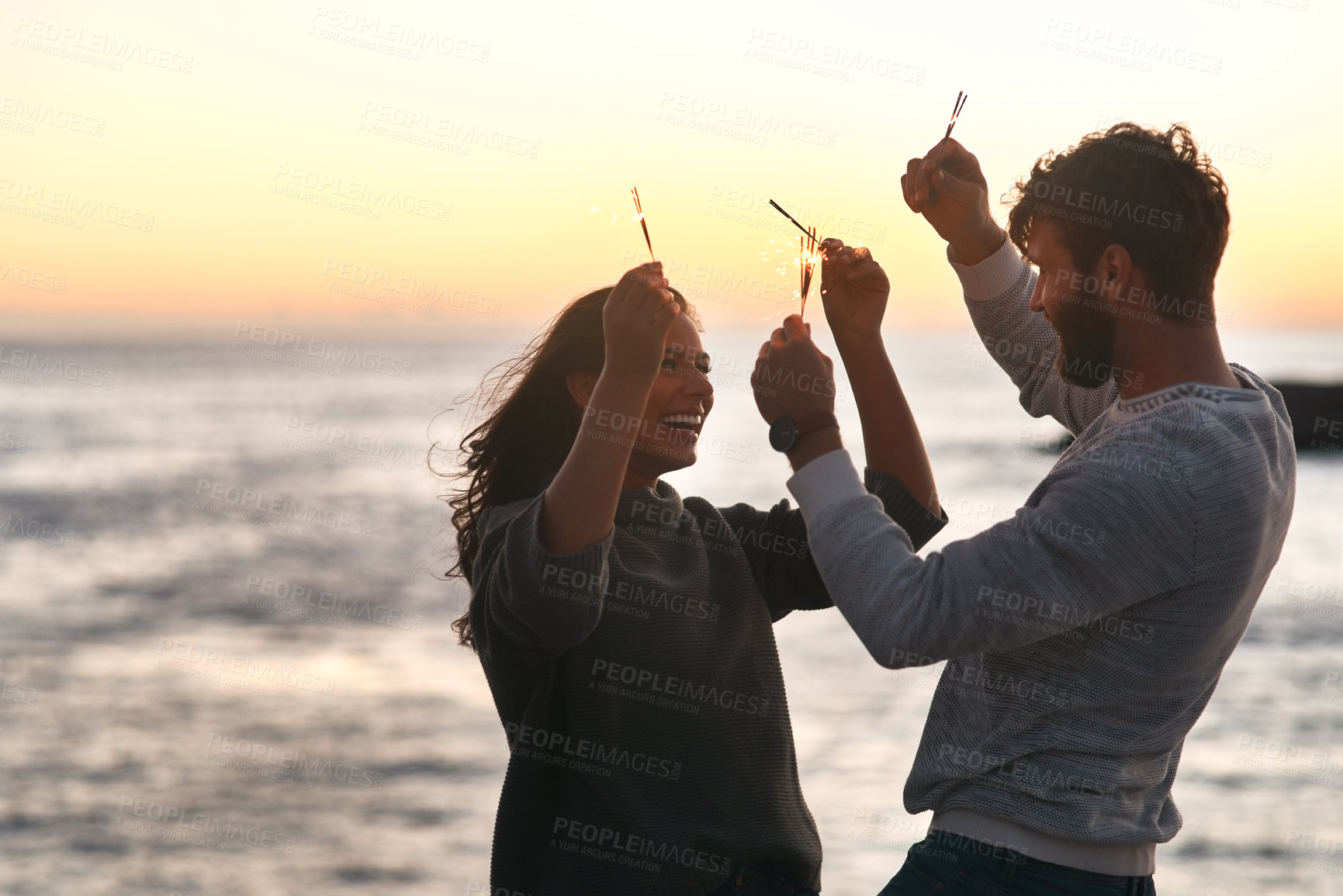 Buy stock photo Sunset, beach and couple with sparklers for celebration, party and quality time on romantic date. Nature, love and happy man and woman with fireworks for honeymoon on holiday, weekend and vacation