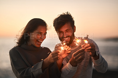 Buy stock photo Shot of a happy young couple having fun with sparklers on the beach at sunset