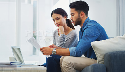 Buy stock photo Cropped shot of a young couple sitting on the sofa while going through paperwork in their lounge