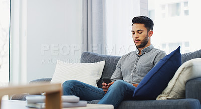 Buy stock photo Cropped shot of a handsome young man sitting on the sofa and using his cellphone while in the lounge