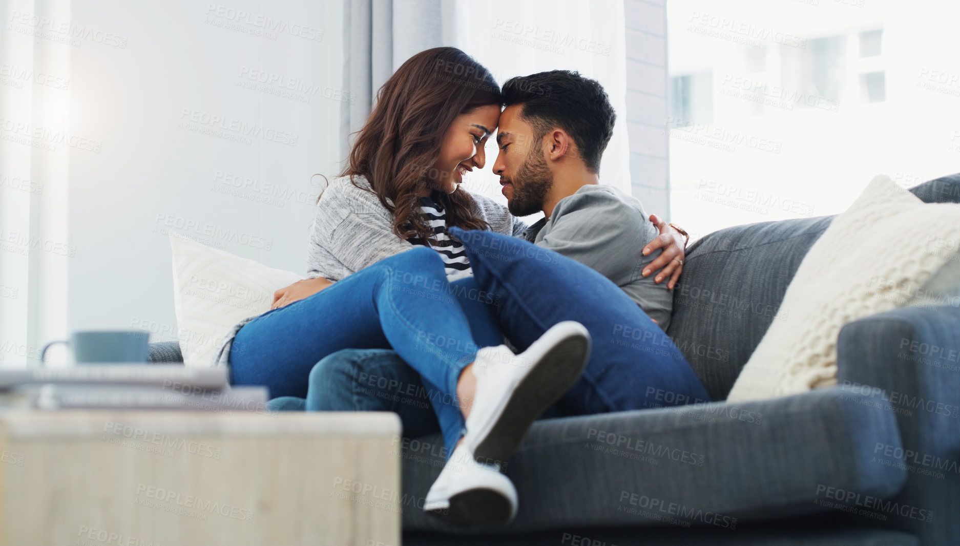 Buy stock photo Cropped shot of an affectionate young couple cuddling with each other while in their living room during the day