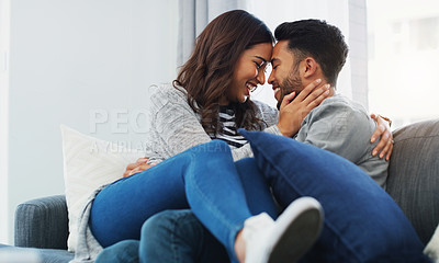 Buy stock photo Cropped shot of an affectionate young couple cuddling with each other while sitting on their sofa during the day