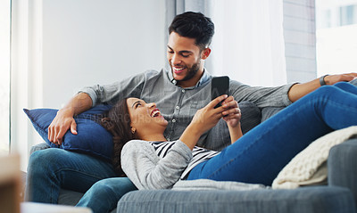 Buy stock photo Cropped shot of an affectionate young couple lounging on the sofa while using a cellphone in their living room
