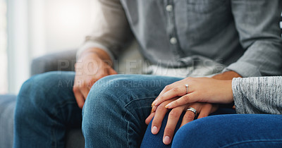 Buy stock photo Cropped shot of an unrecognizable couple holding hands while sitting on the sofa in their living room during the day