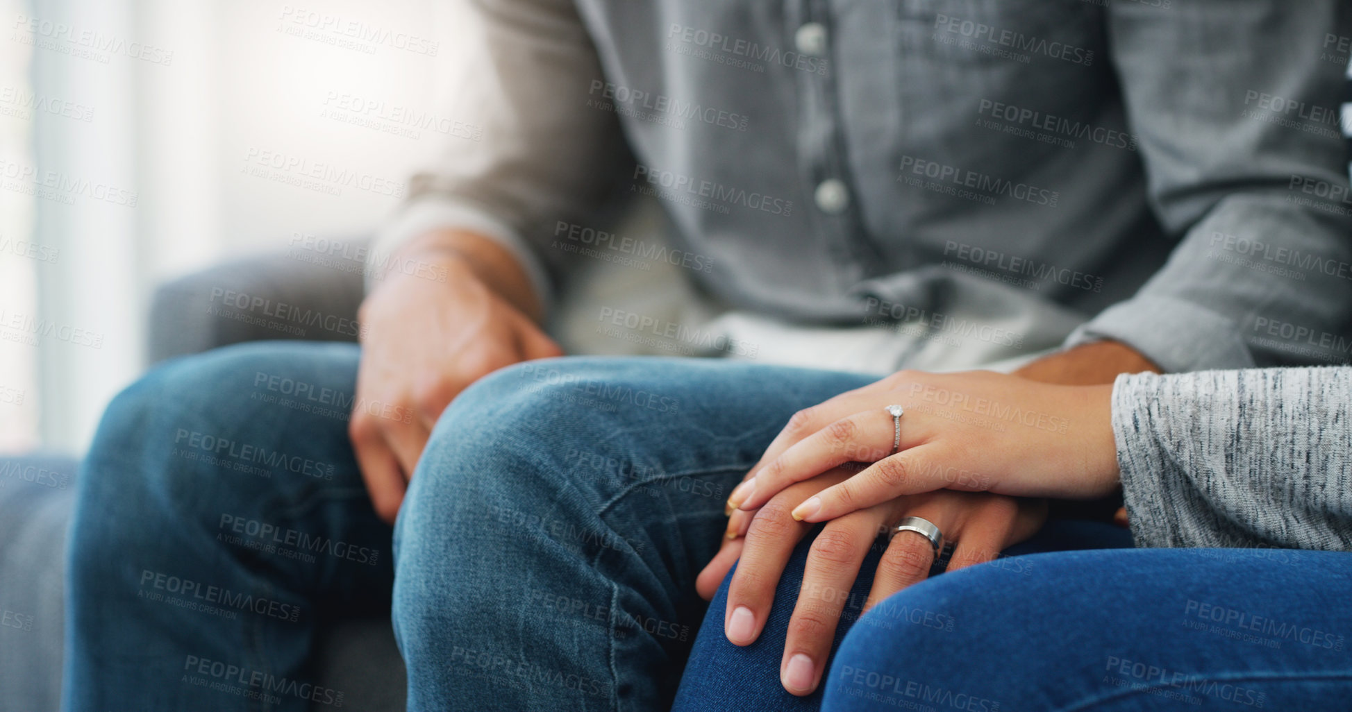 Buy stock photo Cropped shot of an unrecognizable couple holding hands while sitting on the sofa in their living room during the day