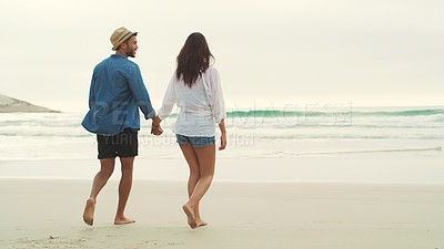 Buy stock photo Full length rearview shot of an affectionate young couple walking alongside each other on the beach during the day