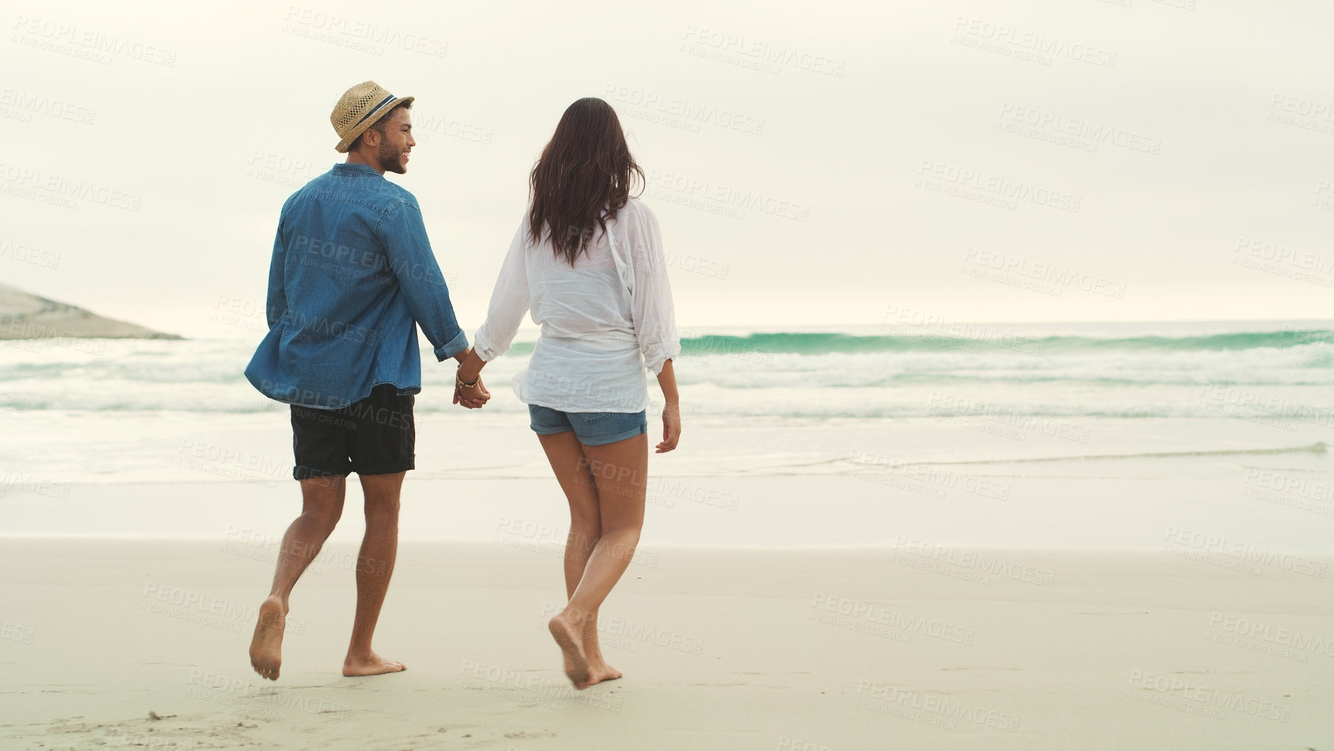 Buy stock photo Full length rearview shot of an affectionate young couple walking alongside each other on the beach during the day