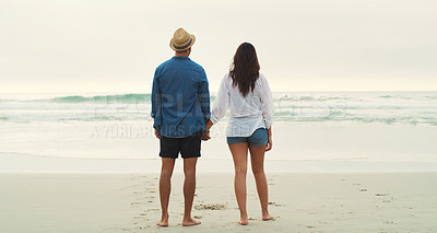 Buy stock photo Full length rearview shot of an affectionate young couple walking alongside each other on the beach during the day