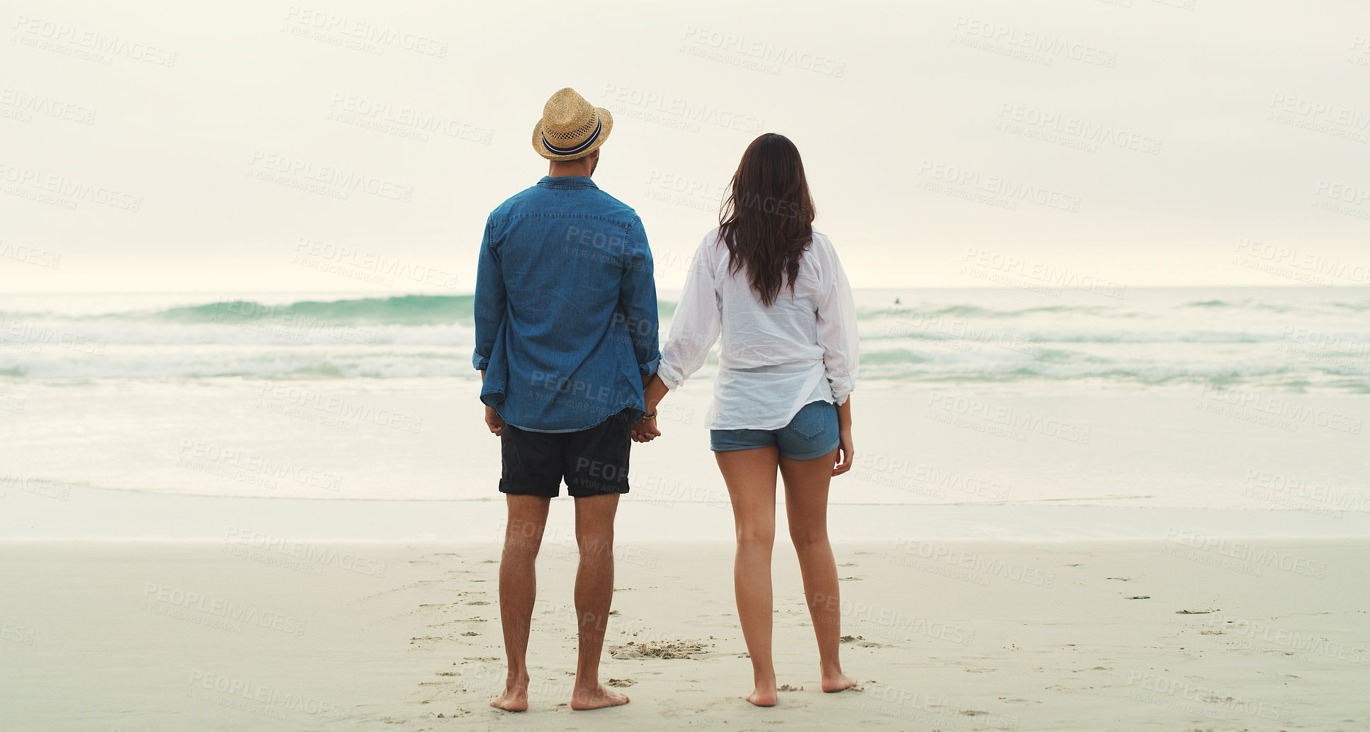 Buy stock photo Full length rearview shot of an affectionate young couple walking alongside each other on the beach during the day