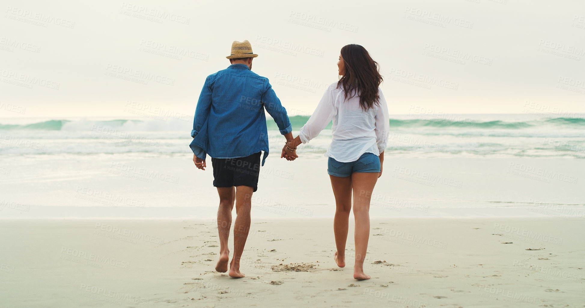 Buy stock photo Full length rearview shot of an affectionate young couple walking alongside each other on the beach during the day