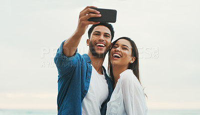 Buy stock photo Cropped shot of a happy young couple posing for a selfie while on the beach during the day