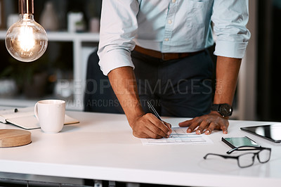 Buy stock photo Shot of an unrecognizable businessman filling out some paperwork while working late in his office