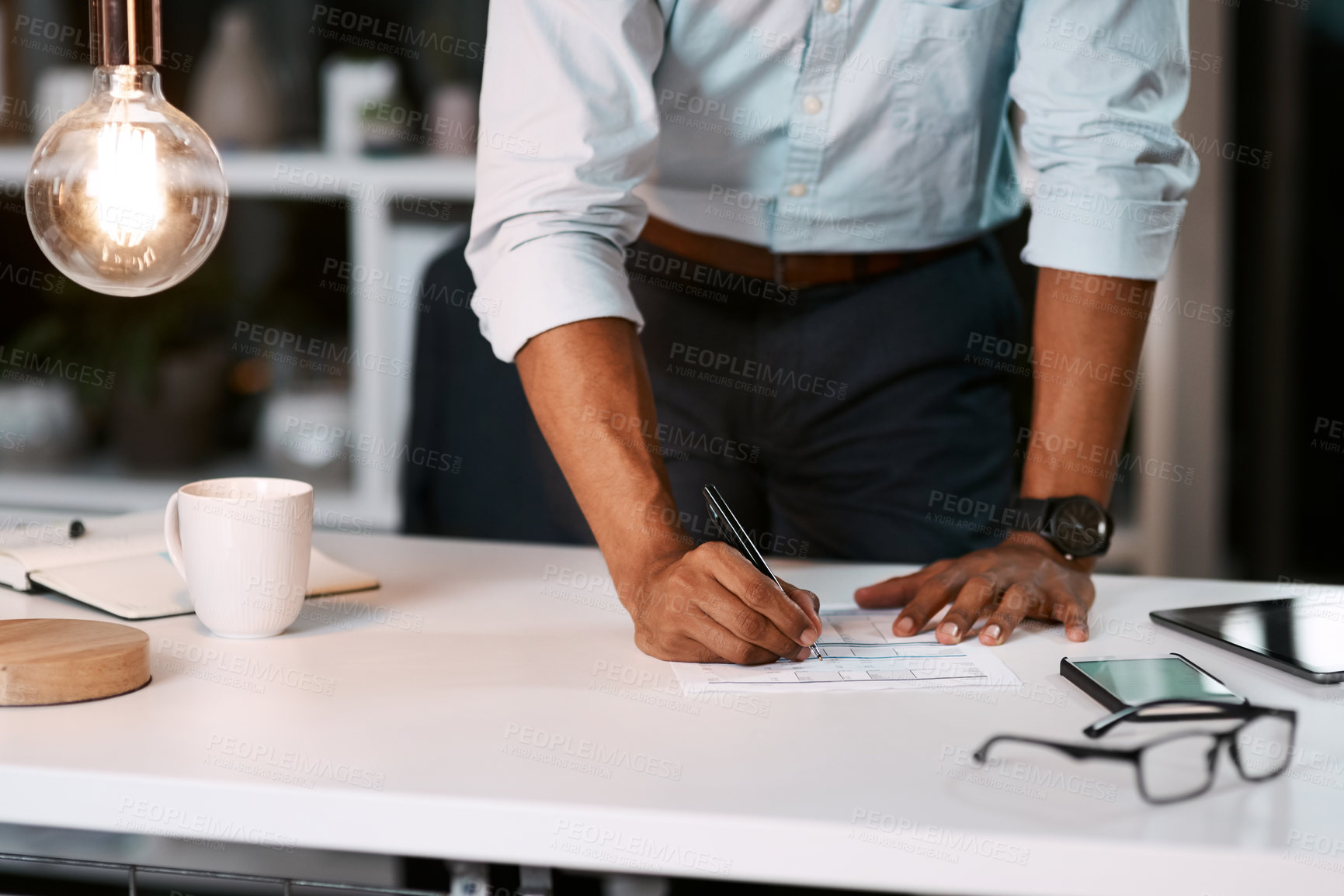 Buy stock photo Shot of an unrecognizable businessman filling out some paperwork while working late in his office