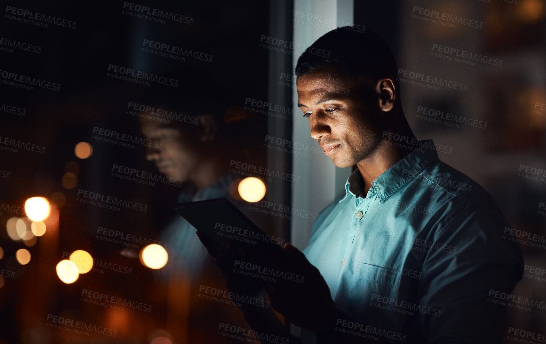 Buy stock photo Shot of a handsome young businessman using a digital tablet while working late in his office