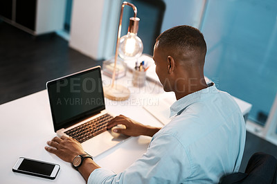 Buy stock photo High angle shot of a young businessman working on his laptop during a late night shift at work