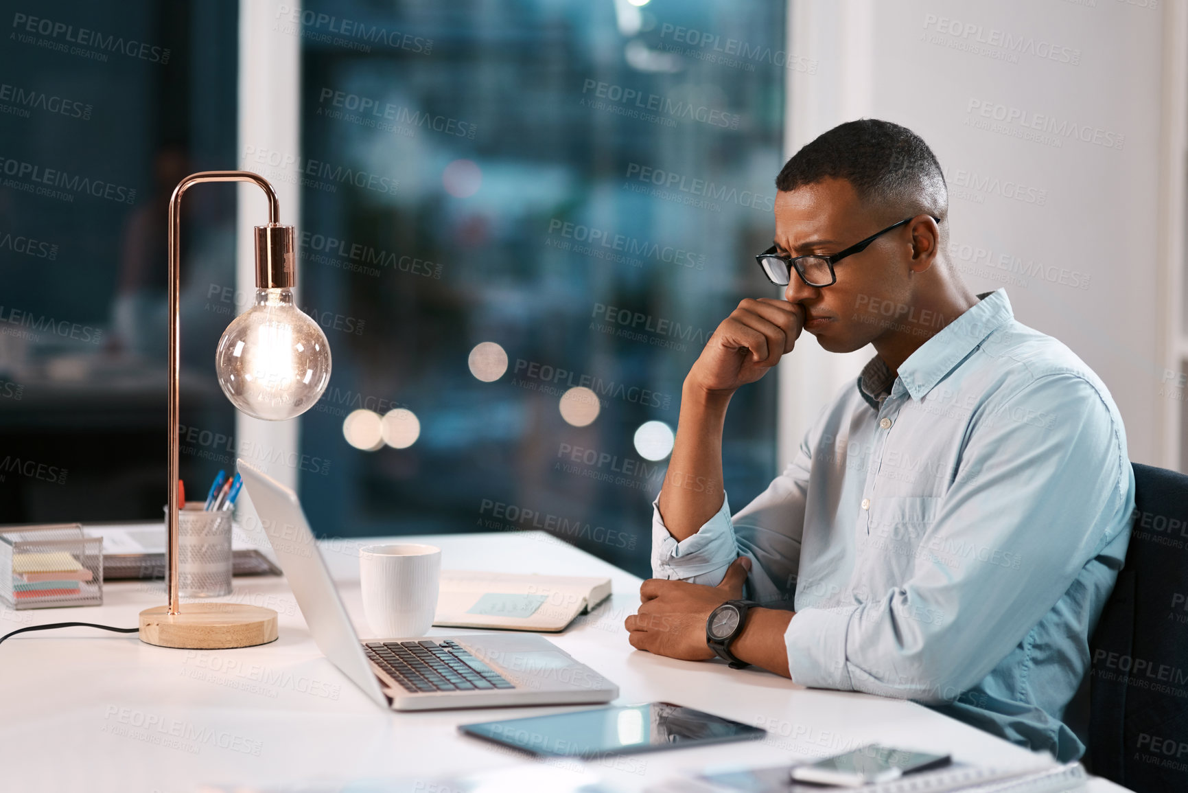 Buy stock photo Shot of a handsome young businessman working on his laptop during a late night shift at work