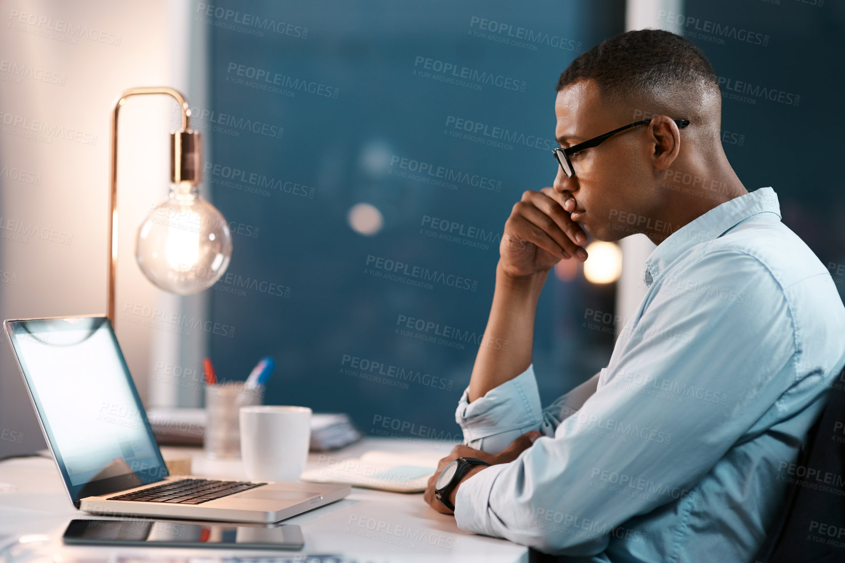 Buy stock photo Shot of a handsome young businessman working on his laptop during a late night shift at work