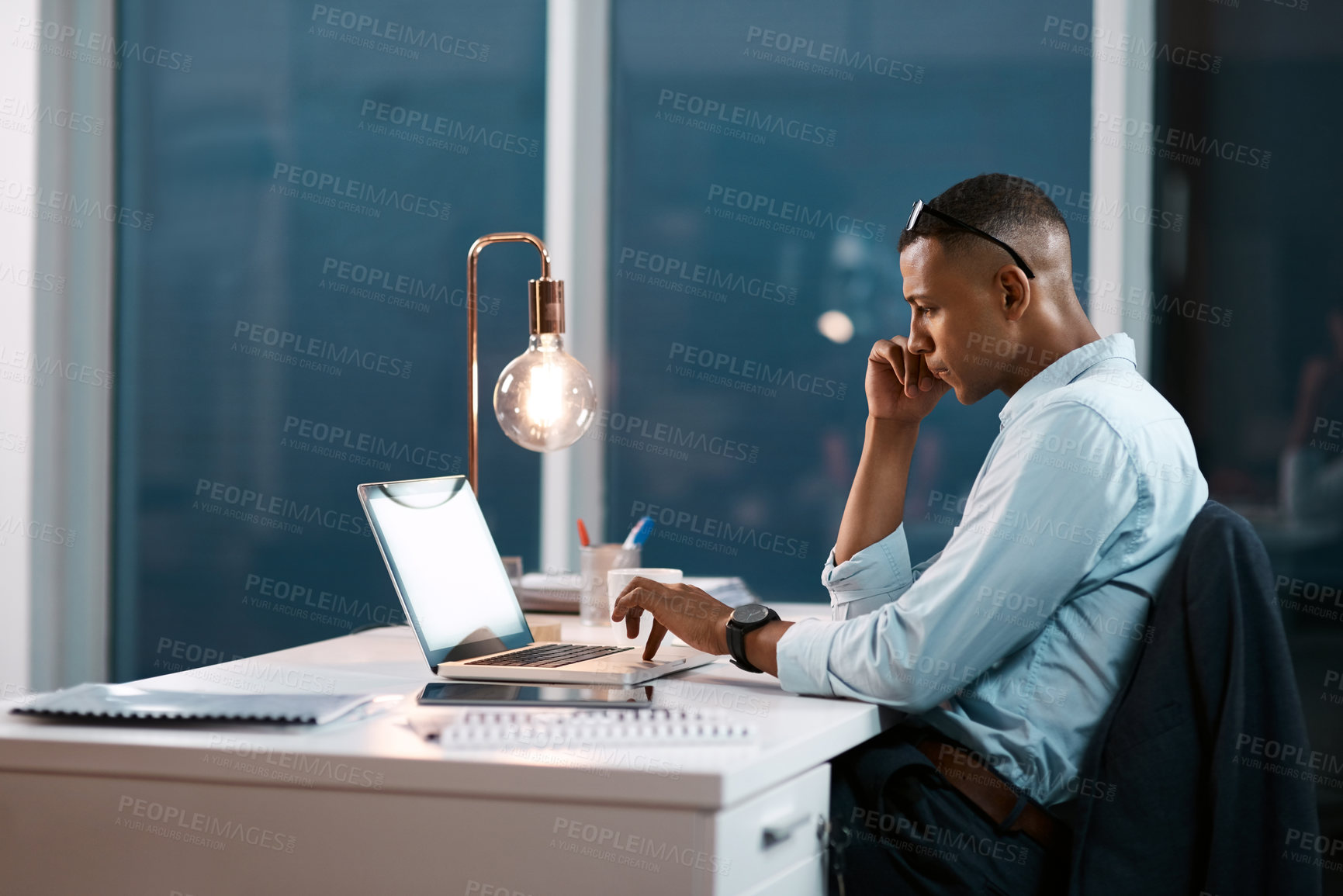 Buy stock photo Shot of a handsome young businessman working on his laptop during a late night shift at work