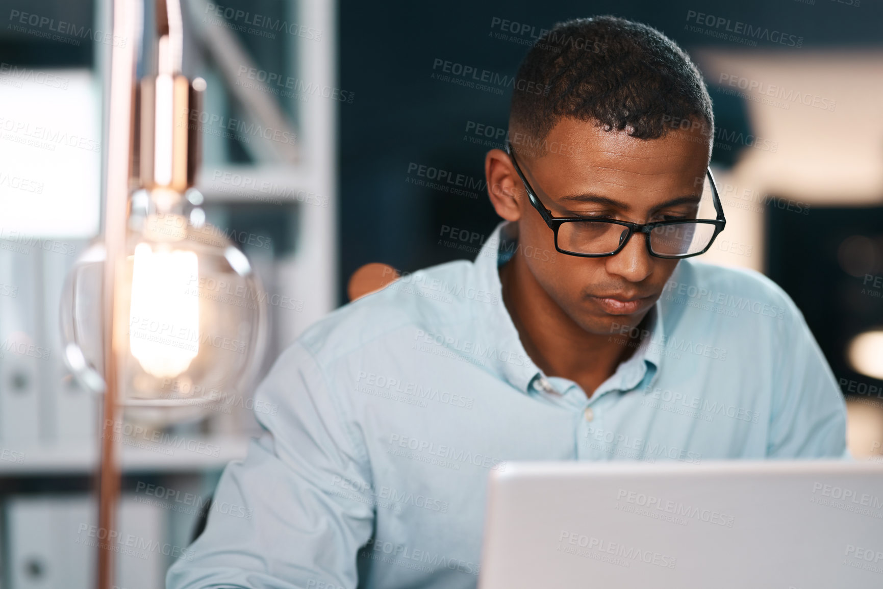 Buy stock photo Shot of a handsome young businessman working on his laptop during a late night shift at work