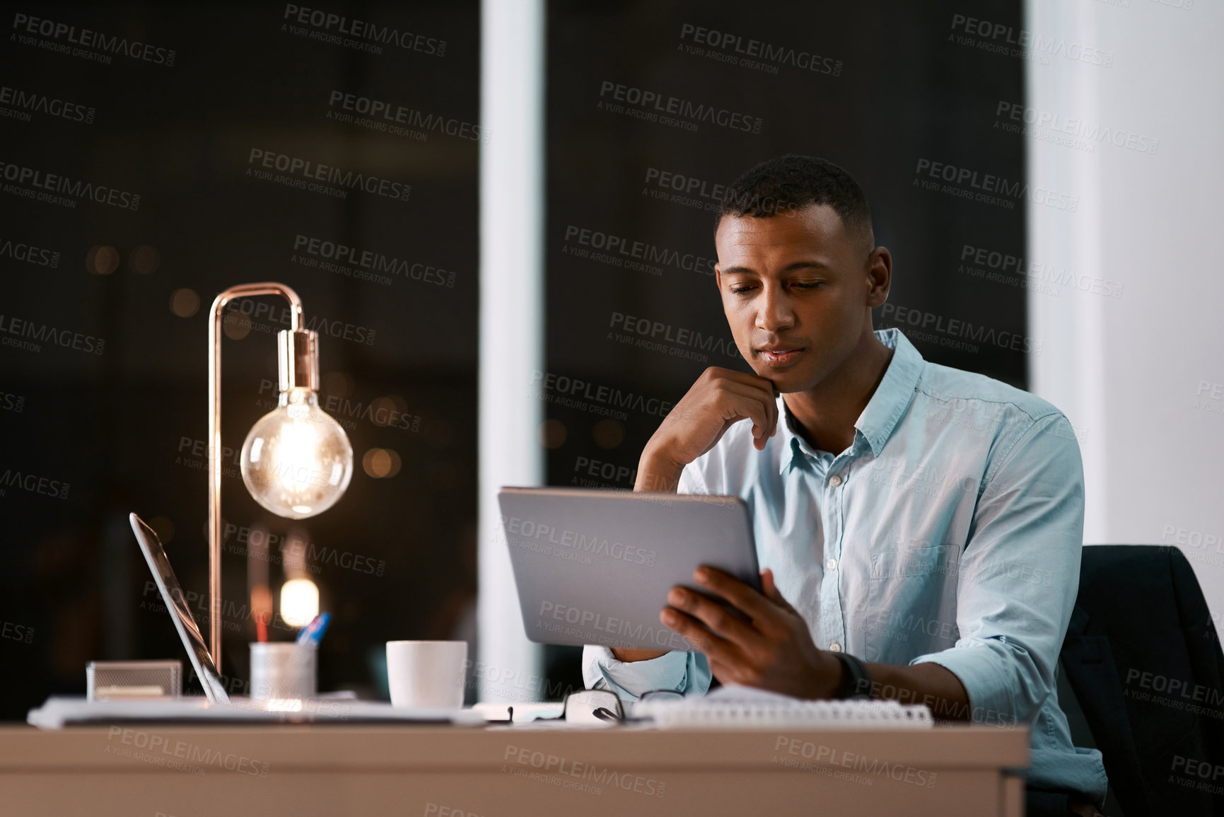 Buy stock photo Shot of a handsome young businessman using a digital tablet while working late in his office