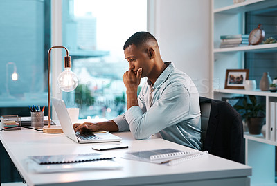 Buy stock photo Shot of a handsome young businessman working on his laptop during a late night shift at work